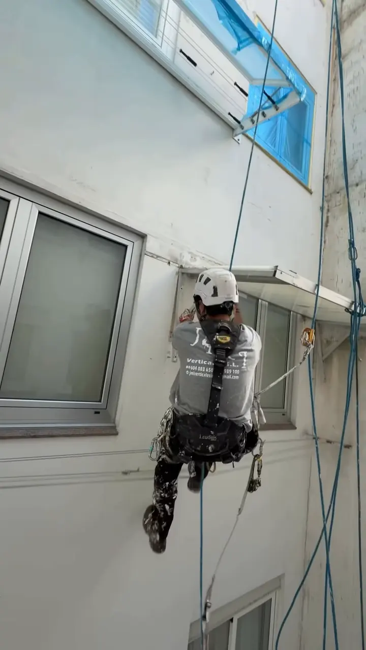 Operario colgado de cuerdas trabajando en la pared de un patio de luces