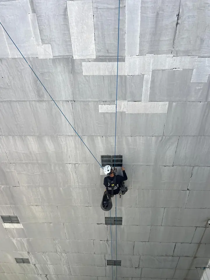 Operario de JMI Verticales colgado de cuerdas sellando ventanas en una fachada
