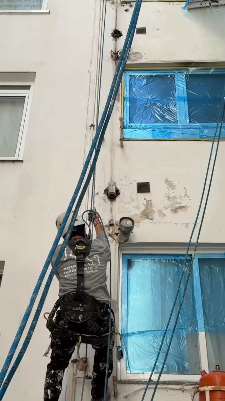 Operario en cuerda trabajando en una tubería de la pared de un patio de luces